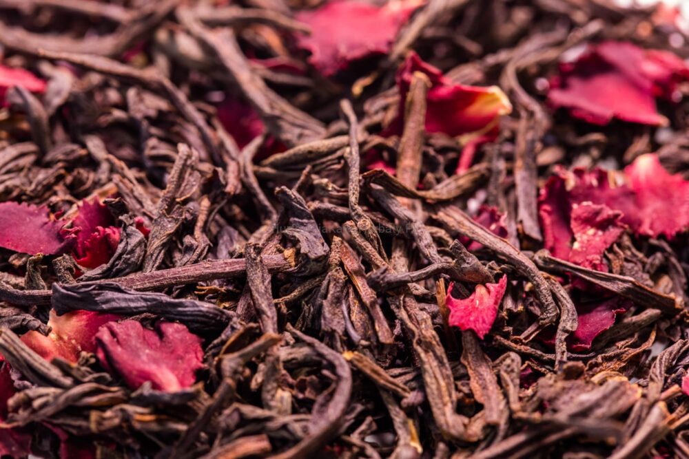 Stos czarnej herbaty z czerwonymi płatkami, tworzący kontrastujące i estetyczne połączenie kolorów.