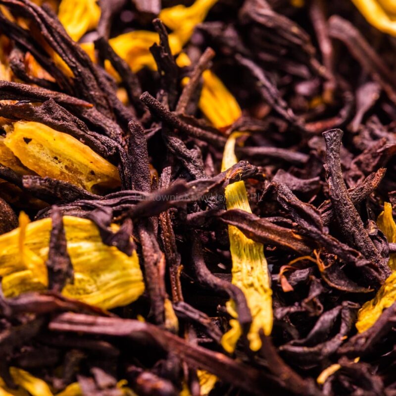 Zbliżenie na stos czarnej herbaty z żółtymi kwiatami, tworzącymi kontrastujące akcenty kolorystyczne.