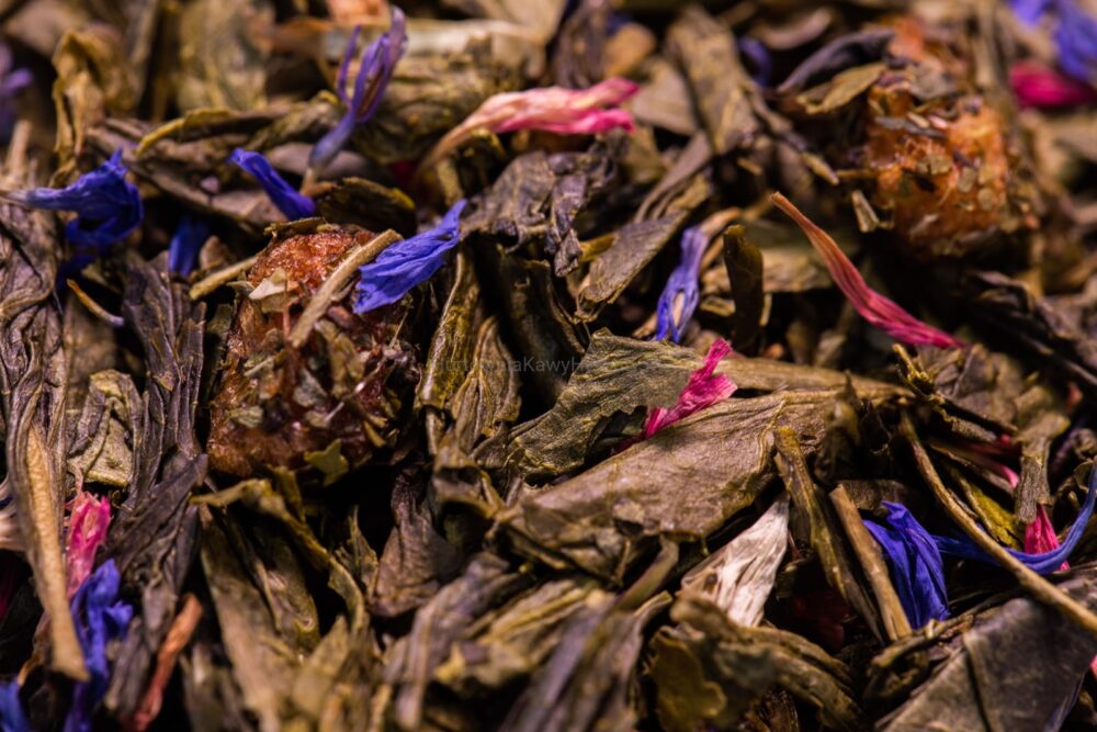 Zbliżenie na zieloną herbatę z niebieskimi i fioletowymi kwiatami, tworzącymi harmonijną kompozycję kolorystyczną.