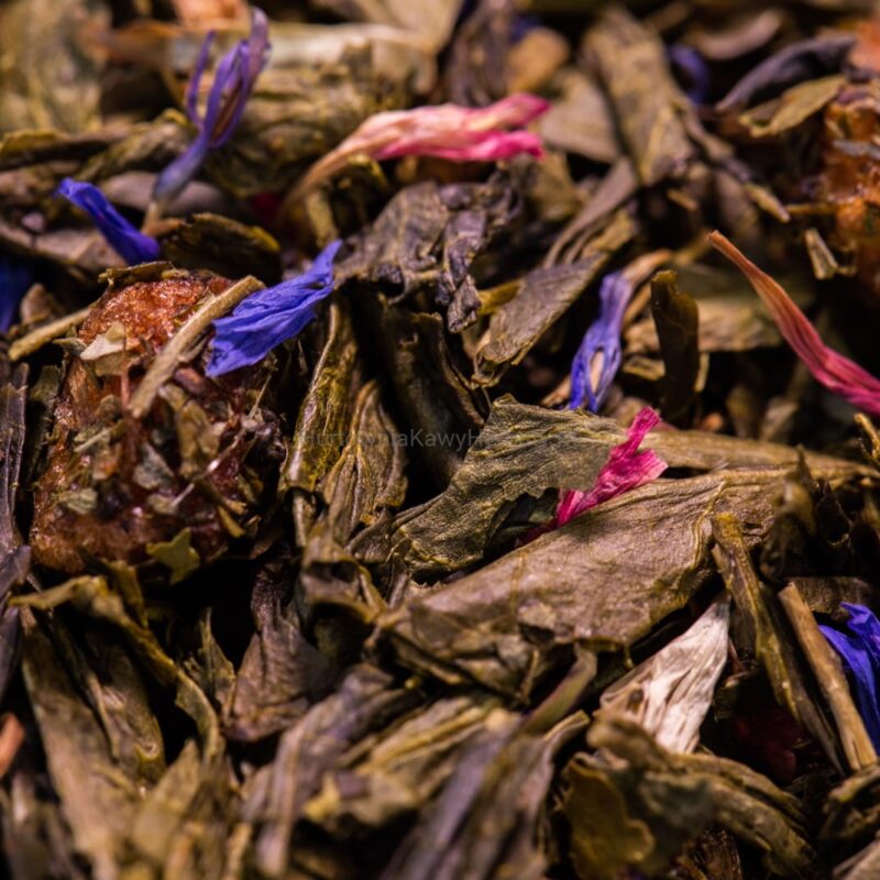 Zbliżenie na zieloną herbatę z niebieskimi i fioletowymi kwiatami, tworzącymi harmonijną kompozycję kolorystyczną.